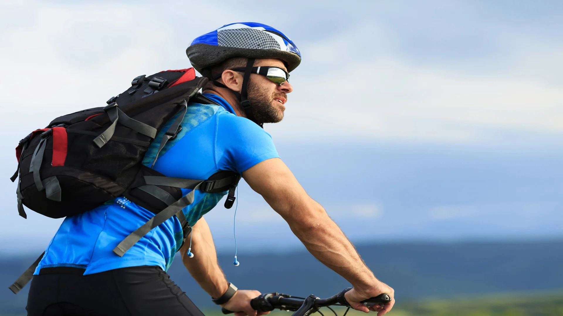 Mann auf Fahrrad mit blauem Helm und blauen T-Shirt. Trägt eine Sonnenbrille und Rucksack.