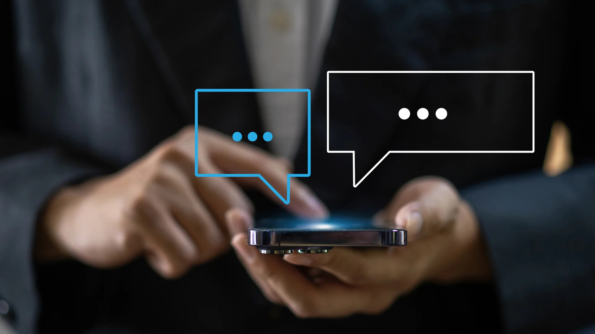 Fotografie zeigt Hände, die Smartphone halten und bedienen, mit zwei Sprechblasen-Symbolen über Gerät. Darstellung symbolisiert digitale Kommunikation oder Messaging in moderner Technologie.
