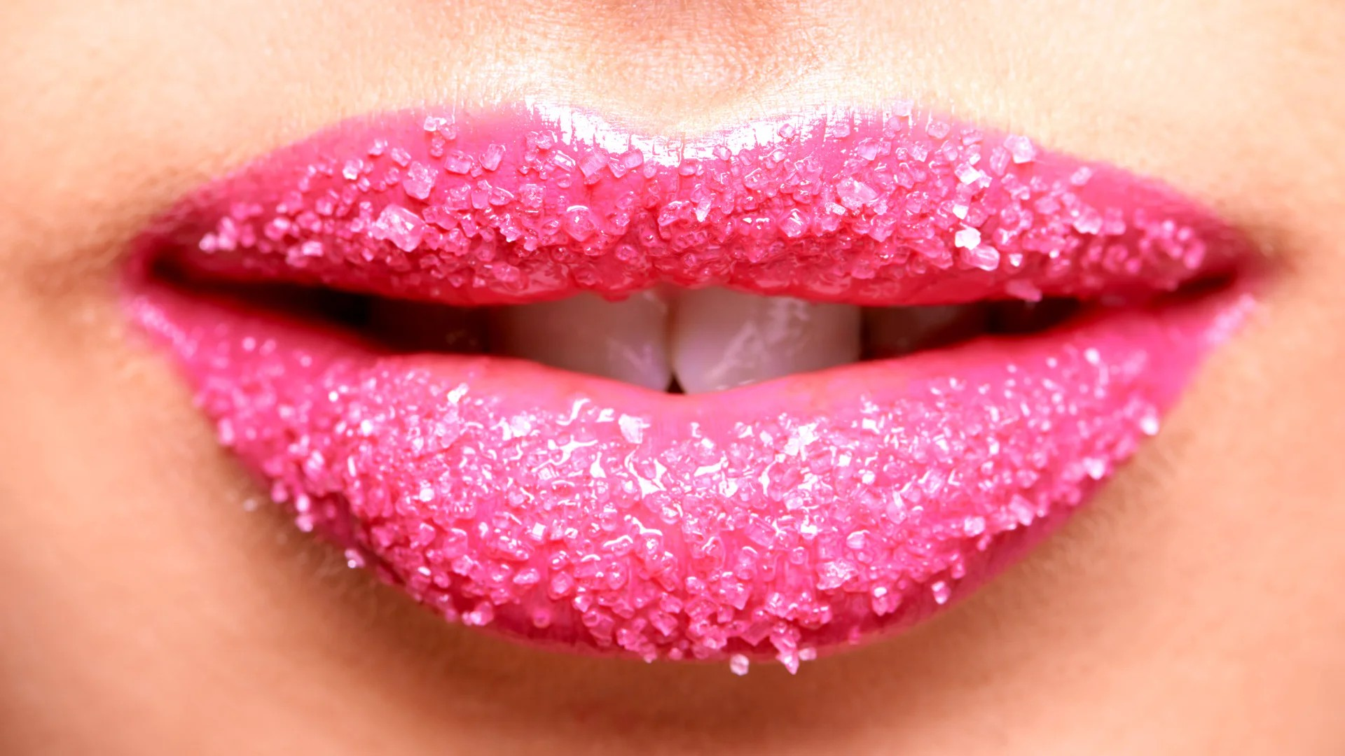 Nahaufnahme von Lippen mit pinkfarbenem Zuckerkristall-Belag, der einen glitzernden Effekt erzeugt. Fokus liegt auf Textur und Farbkontrast zwischen Lippen und Zuckerkristallen.