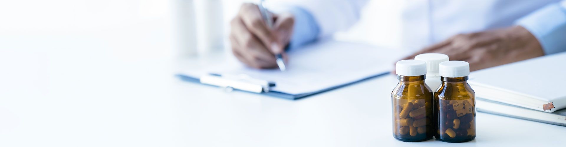 Mann füllt Formular am Schreibtisch aus. Im Fordergrund Medikamentenfläschchen